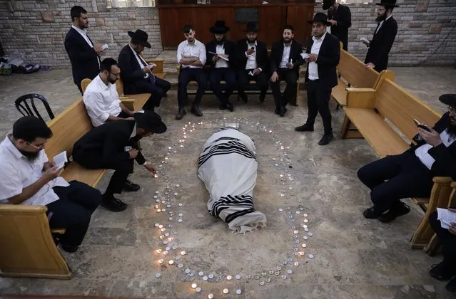 Ultra-Orthodox Jews light candles and pray around the body of Rabbi Shalom Cohen, the spiritual leader of the Shas party, inside a yeshiva in Jerusalem, Israel, 22 August 2022. Rabbi Shalom Cohen died aged 91. The funeral will take place in Jerusalem on 22 August with police expecting tens of thousands of people to attend. (Photo by Abir Sultan/EPA/EFE)