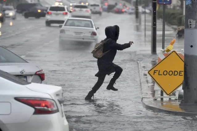 A pedestrian leaps across a flooded portion of the La Paz and Seventh Street intersection as a winter storm arrived, Thursday, December 6, 2018 in Victorville, Calif. The second round of a fall storm dumped snow and rain that jammed traffic on Southern California highways and loosened hillsides in wildfire burn areas on Thursday. (Photo by James Quigg/The Daily Press via AP Photo)