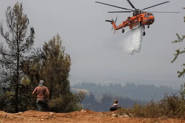 An helicopter drops water over a fire in Galatsonas village on Evia island, about 184 kilometers (115 miles) north of Athens, Greece, Wednesday, August 11, 2021. (Photo by Lefteris Pitarakis/AP Photo)