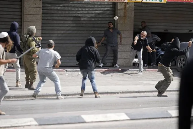A Palestinian man throws a stone at Israeli settlers and an Israeli soldier during clashes in Huwara, near the West Bank town of Nablus, Thursday, October 13, 2022. (Photo by Majdi Mohammed/AP Photo)