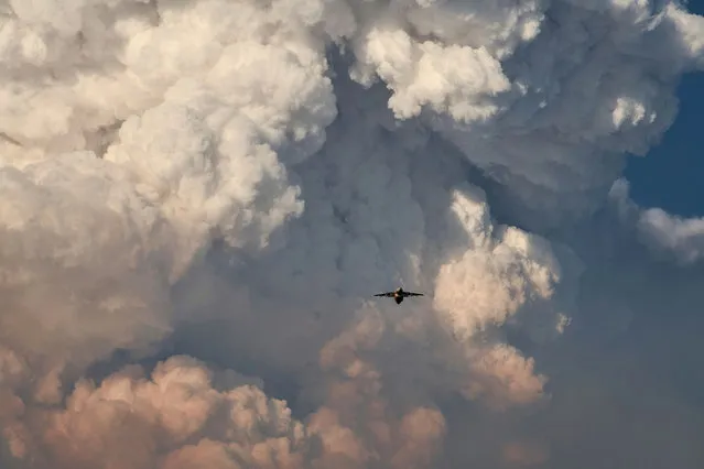 A firefighting aircraft returns to base amid massive plumes of smoke after dropping flame-retarding chemicals on the Bootleg Fire, as it expands to over 225,000 acres, in Bly, Oregon, U.S., July 15, 2021. Picture taken July 15, 2021. (Photo by Mathieu Lewis-Rolland/Reuters)