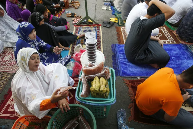 An enterprising Filipino Muslim brings out her sweets as she prepares to pray outside the Blue Mosque in observance of Eid al-Adha, the second most important holiday in the Muslim world, Tuesday, August 21, 2018 in suburban Taguig city, east of Manila, Philippines. Eid al-Adha or the Feast of Sacrifice is marked in the Philippines with prayers and the slaughter of goats and cows and their meat being given to the poor. (Photo by Bullit Marquez/AP Photo)