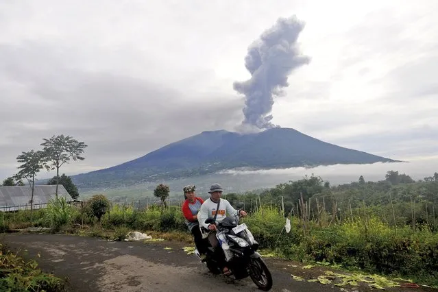 Motorists ride past by as Mount Marapi spews volcanic materials during its eruption in Agam, West Sumatra, Indonesia, Monday, December 4, 2023. The volcano spewed thick columns of ash as high as 3,000 meters (9,800 feet) into the sky in a sudden eruption Sunday and hot ash clouds spread several miles (kilometers). (Photo by Ardhy Fernando/AP Photo)