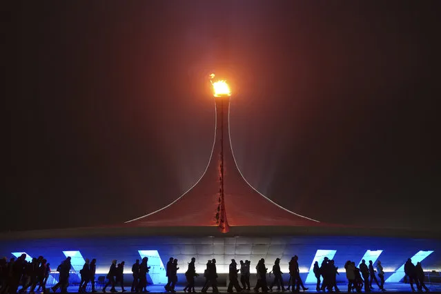 Spectators walk past the Olympic flame on a foggy night in Olympic Park during the 2014 Winter Olympics on Sunday, February 16, 2014, in Sochi, Russia. (Photo by J. David Ake/AP Photo)