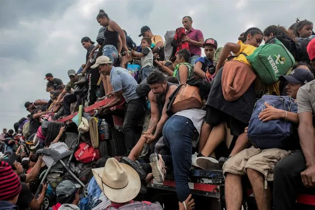 Migrants help fellow migrants onto the bed of a trailer in Jesus Carranza, in the Mexican state of Veracruz, Wednesday, November 17, 2021. (Photo by Felix Marquez/AP Photo)
