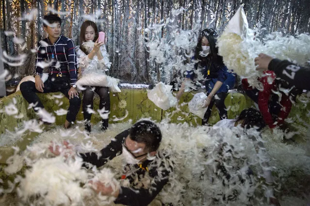 A woman takes a selfie as others fight each other during a pillow fight event in Beijing, China, Saturday, April 2, 2016. Dozens of participants battled each other with feather pillows as a part of a promotional event at the bar. (Photo by Ng Han Guan/AP Photo)