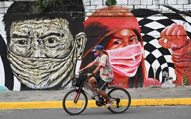 A resident cycles past a mural depicting frontline health workers wearing masks, along a street in Manila on November 10, 2021. (Photo by Ted Aljibe/AFP Photo)