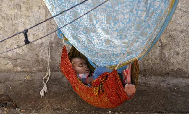 A child sleeps in a hammock along a sidewalk on a hot summer day in Ahmedabad, India, April 19, 2016. (Photo by Amit Dave/Reuters)