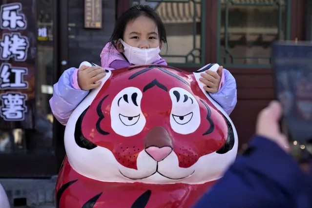 A child wearing a mask holds on to the ears of a Tiger sculpture on the first day of the Lunar Year of the Tiger in Beijing, China, Tuesday, February 1, 2022. (Photo by Ng Han Guan/AP Photo)