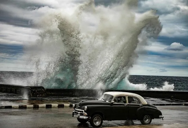 An old American car drives as strong wind pushes a wave in Havana malecon, on February 9, 2022. (Photo by Yamil Lage/AFP Photo)