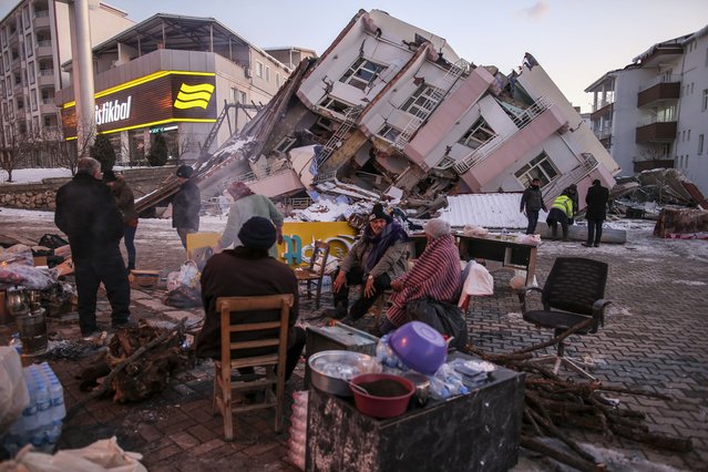 People sit and stand around a collapsed buildings in Golbasi, in Adiyaman province, southern Turkey, Wednesday, February 8, 2023. Thinly stretched rescue teams worked through the night in Turkey and Syria, pulling more bodies from the rubble of thousands of buildings toppled by a catastrophic earthquake. The death toll rose Wednesday to more than 10,000, making the quake the deadliest in more than a decade. (Photo by Emrah Gurel/AP Photo)