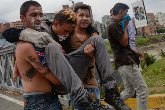Men carry a fellow demonstrator away from the clashes with the riot police during a protest against Venezuelan President Nicolas Maduro, in Caracas on April 20, 2017. (Photo by Federico Parra/AFP Photo)