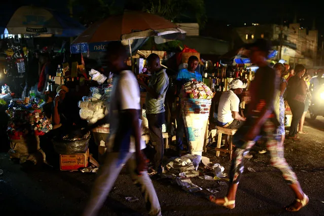 In this April 16, 2019 photo, vendors sit at a street corner as people walk past them, at night in Petion-Ville, Haiti. Since the blackouts hit Haiti, nighttime activity has ground to a halt as armed robbers hold up street merchants or break into people's homes in darkness. (Photo by Dieu Nalio Chery/AP Photo)