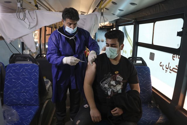 A man receives a COVID-19 vaccine at a mobile vaccine clinic bus at the Grand Bazaar of Tehran, Iran, Saturday, January 22, 2022. After successive virus waves pummeled the country for nearly two years, belated mass vaccination under a new, hard-line president has, for a brief moment, left the stricken nation with a feeling of apparent safety. (Photo by Vahid Salemi/AP Photo)