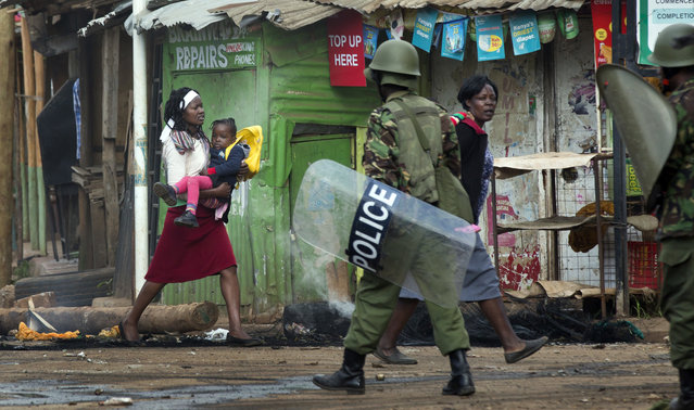 A woman takes advantage of a lull in the clashes to carry her baby to safety, as police firing tear gas engage protesters throwing rocks in the Kibera slum of Nairobi, Kenya Monday, May 23, 2016. (Photo by Ben Curtis/AP Photo)