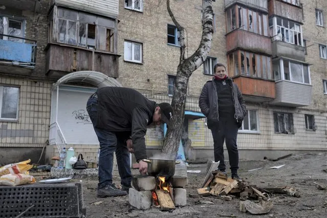 Oleksander Radkevich, 41, cooks on a makeshift fire next to his wife Irina Shekhovtsova outside their destroyed apartment building in the town of Borodyanka, Ukraine, on Saturday, April 9, 2022. Russian troops occupied the town of Borodyanka for weeks. Several apartment buildings were destroyed during fighting between the Russian troops and the Ukrainian forces in the town around 40 miles northwest of Kiev. (Photo by Petros Giannakouris/AP Photo)