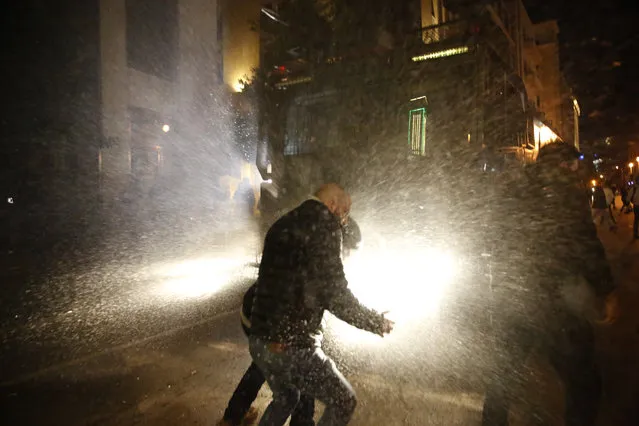 Anti-government protesters are sprayed by water form the riot police, during a protest near the parliament square, in downtown Beirut, Lebanon, Sunday, December 15, 2019. Lebanese security forces fired tear gas, rubber bullets and water cannons Sunday to disperse hundreds of protesters for a second straight day, ending what started as a peaceful rally in defiance of the toughest crackdown on anti-government demonstrations in two months. (Photo by Hussein Malla/AP Photo)