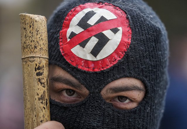 A protester wears a mask adorned with an anti-Nazi symbol during protests marking the 48th anniversary of the 1973 military coup and the death of Chile's late President Salvador Allende, in Santiago, Chile, Saturday, September 11, 2021. The coup ousting the democratically elected leader, Allende, began the dictatorship of Gen. Augusto Pinochet. (Photo by Esteban Felix/AP Photo)