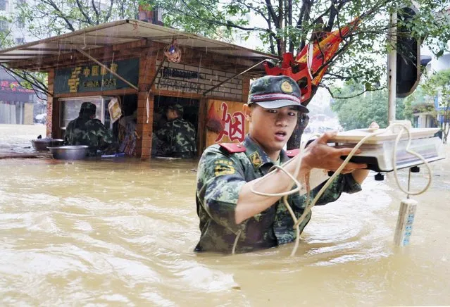 A paramilitary policeman walks among floodwater as he transports residents' belongings to safety amid heavy rainfalls in Tongren, Guizhou province July 15, 2014. Rainstorms lashed China's Hunan Province and Guizhou Province on Monday and Tuesday, affecting over 1 million people, Xinhua News Agency reported. (Photo by Reuters/Stringer)