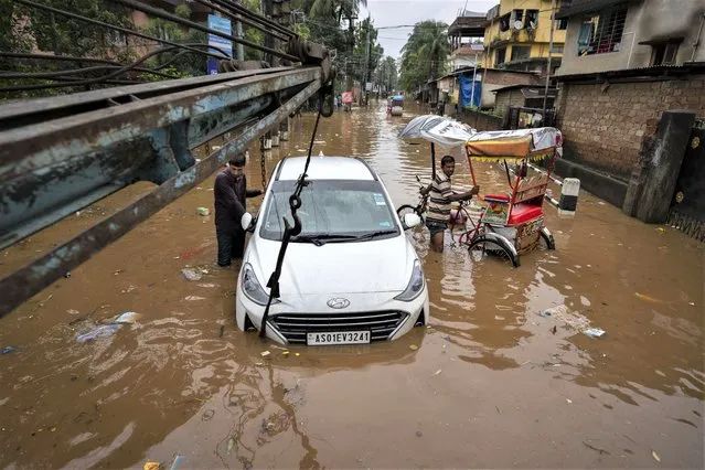 A man stands near his car stranded in a waterlogged street after continuous rainfall in Gauhati, India, Wednesday, June 15, 2022. (Photo by Anupam Nath/AP Photo)