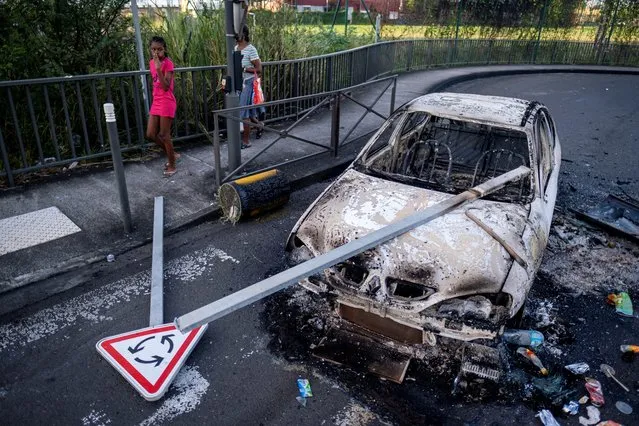 A girl reacts as she walks past a street barricade with a burned car after unrest triggered by coronavirus disease (COVID-19) curbs, which has already rocked the nearby island of Guadeloupe, in Fort-De-France, Martinique on November 26, 2021. (Photo by Ricardo Arduengo/Reuters)