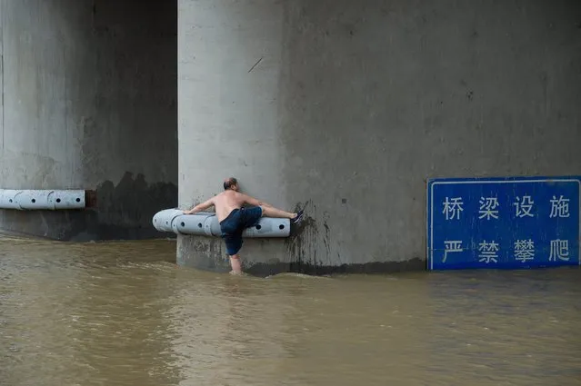 A picture made available 05 July 2016 shows a man trying to climb a pier on a bridge across the Hanjiang River in Wuhan, Hubei province, China, 04 July 2016. Heavy rains have caused flooding in provinces in the middle and lower sections of the Yangtze River. (Photo by Mei Xin/EPA)