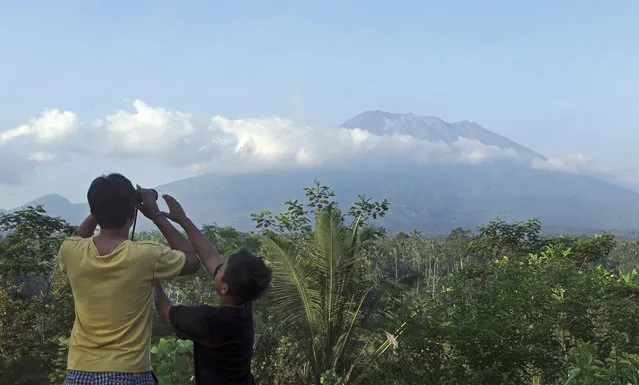 In this September 20, 2017, file photo, a man looks out at Mount Agung with binoculars at an observation point in Bali, Indonesia. Authorities have ordered the evacuation of villagers living within a high danger zone that in places extends 12 kilometers (7.5 miles) from Mount Agung's crater. But people further away are also leaving. (Photo by Firdia Lisnawati/AP Photo)