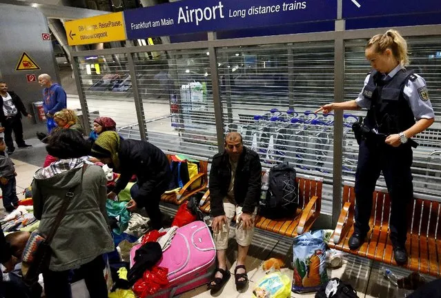 A German border policewoman stands on a bench while talking to migrants who unexpectedly disembarked a train that departed from Budapest's Keleti station, at the railway station of the airport in Frankfurt, Germany, early morning September 6, 2015. (Photo by Kai Pfaffenbach/Reuters)