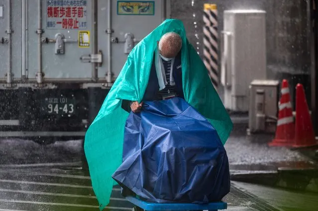 A staff member works under heavy rain brought about by Typhoon Nanmadol, in Ueno district of Tokyo on September 18, 2022. (Photo by Philip Fong/AFP Photo)