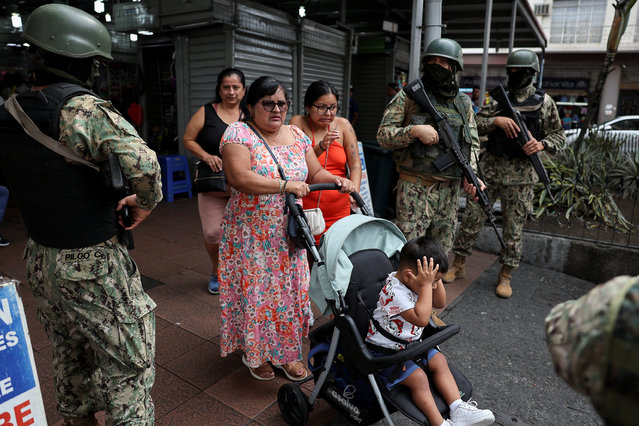 People walk past armed soldiers, as they guard a commercial area, in the aftermath of a wave a violence that saw the storming of a TV station on-air and explosions around the nation, in Quito, Ecuador on January 11, 2024. (Photo by Ivan Alvarado/Reuters)