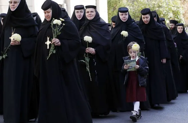 A Romanian school girl walks along a group of Orthodox nuns that carry yellow fresh chrysanthemum flowers while accompanying the relics of Saint Dimitrie Basarabov, the patron saint of Romania's capital, durnig a procession in front of Patriarchal Cathedral in Bucharest, Romania, 24 October 2022. Romanians will celebrate Saint Dimitrie Basarabov on 27 October 2022. Thousands of pilgrims from all over the country are expected in Bucharest to worship the relics of the patron Saint of Bucharest the next few days. (Photo by Robert Ghement/EPA/EFE)