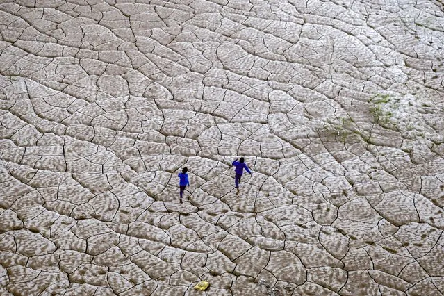 Boys run along the dried-up portion of a riverbed on the banks of river Ganges in Prayagraj, on November 17, 2022. (Photo by Sanjay Kanojia/AFP Photo)