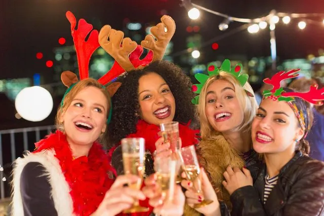 Portrait enthusiastic young women wearing Christmas reindeer antlers and drinking champagne at party. (Photo by Tom Merton/Caiaimage/Getty Images)
