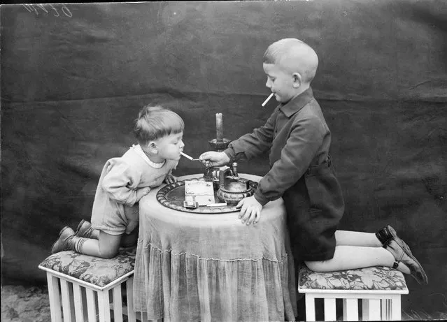 Two young boys kneel on stools on either side of a round table as one uses a match to this the other's cigarette, November 12, 1928. (Photo by FPG/Getty Images)