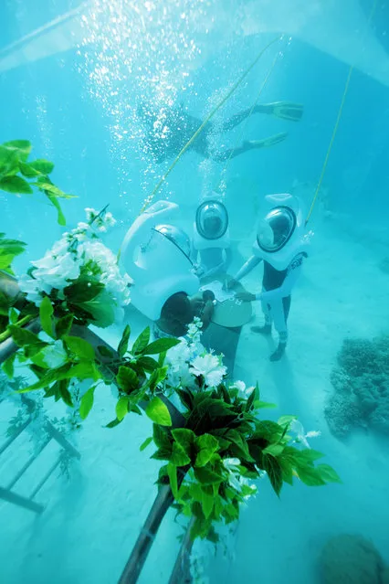 In a picture taken with an underwater camera, a couple stands in front of a Polynesian priest during their underwater wedding ceremony on October 25, 2014 in Bora-Bora, in French Polynesia. The ceremony lasts twenty minutes and costs around 2700 euros. (Photo by Ben Thouard/AFP Photo)
