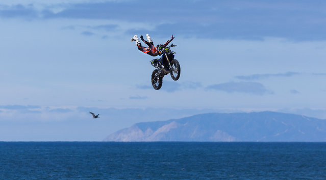 Freestyle motocross rider Taka Higashino, originally from Japan but now lives in Temecula, does a no-hands superman trick high over the beach along with a seagull in flight with a view of Catalina Island as he and a fellow freestyle motocross riders perform aerial acrobatics on the opening day of competition at the U.S. Open of Surfing, which continues through August 3 in Huntington Beach Saturday, on July 26, 2025. (Photo by Allen J. Schaben/Los Angeles Times via Getty Images)