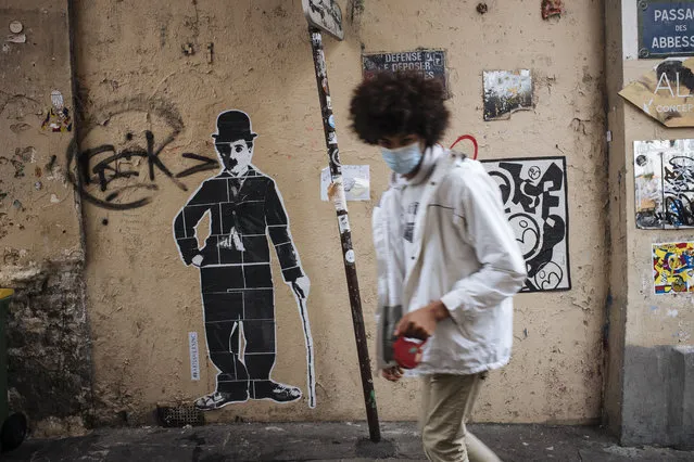 A man wearing a face mask, walks by a Charlie Chaplin street art, in the Montmartre district of Paris, Sunday October 25, 2020. A curfew intended to curb the spiraling spread of the coronavirus, has been imposed in many regions of France including Paris and its suburbs. (Photo by Lewis Joly/AP Photo)