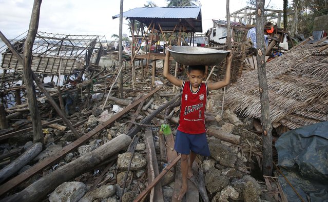A boy carries on his head a metal container containing rice past houses destroyed during the onslaught of Typhoon Hagupit in San Julian, eastern Samar, in central Philippines December 9, 2014. (Photo by Erik De Castro/Reuters)