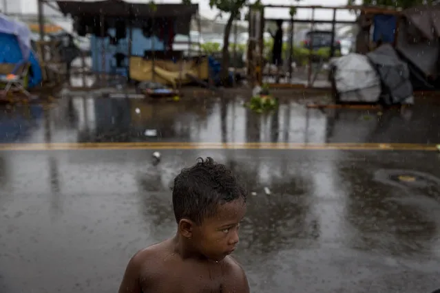 In this Wednesday, August 26, 2015 photo, a boy stands in the rain in front of makeshift tents at a homeless encampment in the Kakaako district of Honolulu. Micronesians made up about a third of the Kakaako homeless encampment. (Photo by Jae C. Hong/AP Photo)