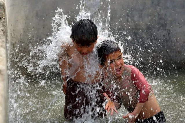 Boys play under a water tap in Jalalabad, Afghanistan on March 15, 2023. (Photo by Shafiullah Kakar/AFP Photo)