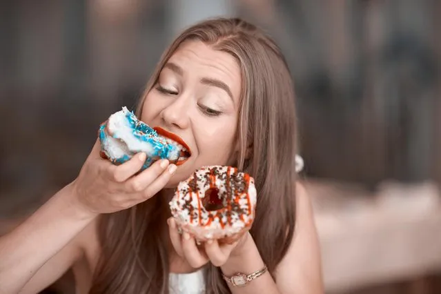Cute young woman holding donuts and biting it.cravinf for sweets.Horizontal lifestyle shot. (Photo by Stock_colors/Getty Images)