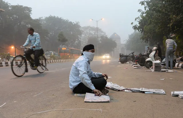An Indian newspaper vendor wears a mask whilst he sorts news papers on a road as heavy smog covers New Delhi on November 7, 2016. Schools in the Indian capital will be closed for the next three days, the Delhi state government said on November 6, as the city struggles with one of the worst spells of air pollution in recent years. (Photo by Sajjad Hussain/AFP Photo)