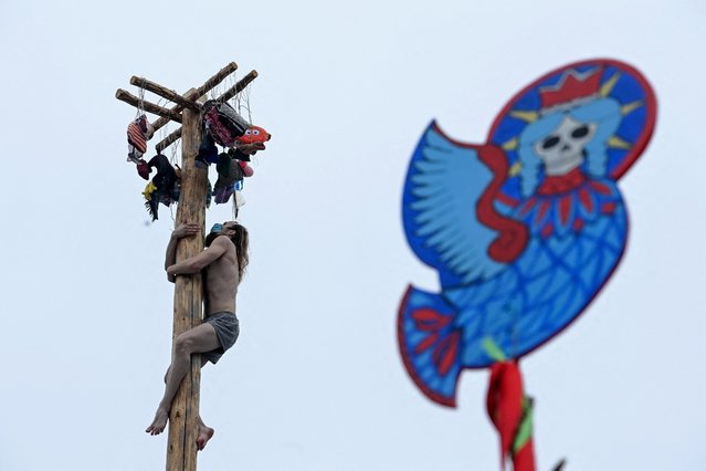A man wearing a protective mask competes in the pole-climb game as he celebrates the Maslenitsa or Shrovetide, a farewell ceremony to winter close to village of Gzhel about 60 km from Moscow on March 14, 2021. Shrovetide precedes the beginning of Lent, with each day of the week holding its own meaning. Shrove Sunday, also known as the Sunday of Forgiveness, is a day for asking forgiveness for the harm caused to other people intentionally or unintentionally (Photo by Kirill Kudryavtsev/AFP Photo)