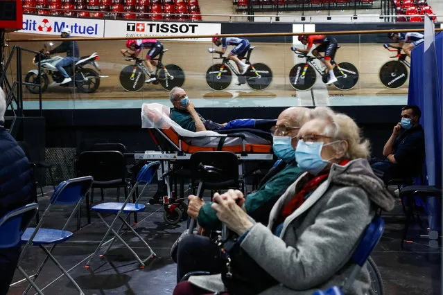 France's national cycling team trains as people wait to get a dose of the “Comirnaty” Pfizer-BioNTech COVID-19 vaccine as part of the coronavirus disease vaccination campaign at the indoor Velodrome National of Saint-Quentin-en-Yvelines in Montigny-le-Bretonneux, southwest of Paris, France, March 26, 2021. (Photo by Gonzalo Fuentes/Reuters)