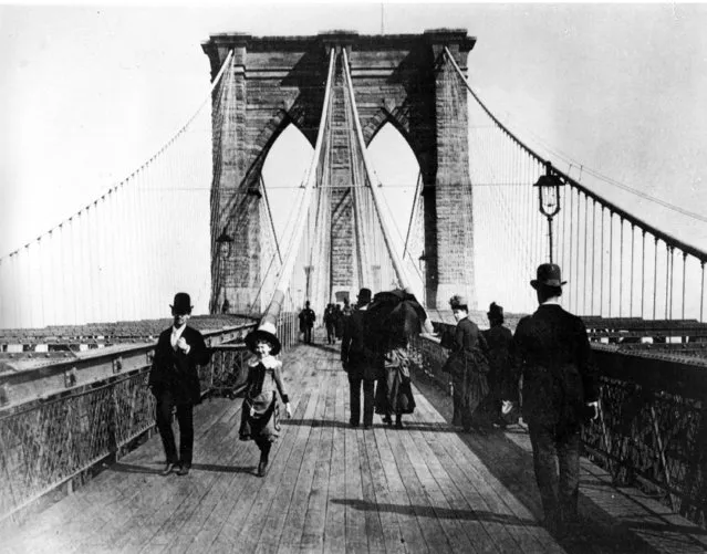 Pedestrians stroll along the promenade of the Brooklyn Bridge, connecting Manhattan and Brooklyn, New York City, 1891. The suspension bridge was opened to traffic on May 24, 1883. When bridge designer John A. Roebling incorporated the promenade into the design of the bridge, he said it was important that the people take part in the leisures afforded by the bridge. (Photo by AP Photo)