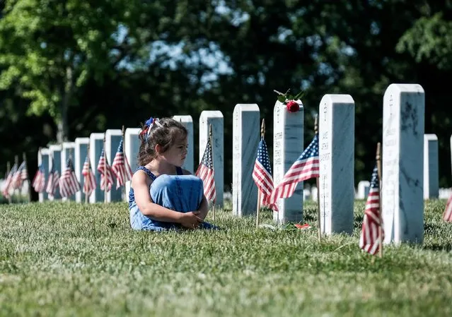 A girl sits in front of a headstone during Memorial Day as visitors honor veterans and those lost in war at Arlington National Cemetery, Virginia, U.S., May 31, 2021. (Photo by Michael A. McCoy/Reuters)