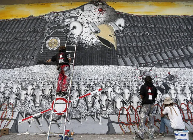 Artists A.Signl, left, and B.Shanti, second from right, of the artist group Captain Borderline paint their mural   “Surveillance of the fittest” at a wall in Cologne, Germany, Thursday, October 24, 2013. The painting shows an American Bald Eagle with surveillance cameras watching a herd of sheep to draw attention to the spying program of the American National Security Agency. Germany demanded answers to “all open questions” about U.S. surveillance Thursday following allegations that American intelligence may have targeted Chancellor Angela Merkel’s cellphone, and her chief of staff noted that Washington hasn’t denied past snooping. (Photo by Frank Augstein/AP Photo)