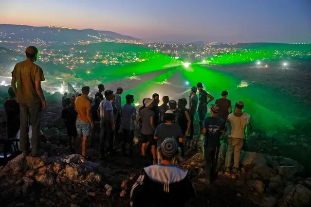 Israeli settlers and supporters in the newly-established wildcat outpost of Eviatar look as Palestinian protestors flash laser beams towards them from the nearby Beita village, near the northern Palestinian city of Nablus in the occupied West Bank, on June 28, 2021. Jewish settlers agreed to leave a new outpost in the occupied West Bank that has stirred weeks of Palestinian protests following a deal with Israel's government, in an agreement confirmed by the interior ministry and settler leaders, under which they will leave the Eviatar outpost within days but their mobile homes will remain and Israeli troops will establish a base in the area. (Photo by Menahem Kahana/AFP Photo)
