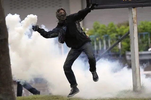Anti-government protester throws back a tear gas canister to riot police, during protest in Bangkok, Thailand, Wednesday, August 11, 2021. Protesters demanded the resignation of Prime Minister Prayuth Chan-ocha for what they say is his failure in handling the COVID-19 pandemic. (Photo by Sakchai Lalit/AP Photo)