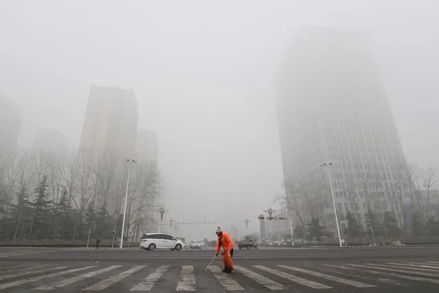 A street cleaner works as fog and air pollution shroud buildings in Qingzhou, in China's eatern Shandong province on December 28, 2023. (Photo by AFP Photo/China Stringer Network)